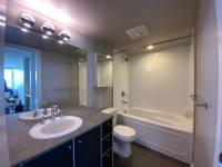 modern bathroom featuring a clean white bathtub and toilet, sleek dark wood vanity with gray countertop, large mirror with contemporary lighting fixtures, and neutral wall tones creating a bright and inviting space with practical amenities.