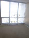 bright and spacious empty room featuring large floor-to-ceiling windows with horizontal blinds, beige carpet flooring, and neutral wall colors, offering abundant natural light and a clean, modern living space with a city view outside.