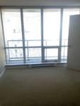 bright empty room with large floor-to-ceiling windows and white blinds allowing ample natural light, beige carpeting, and a simple white door, offering a clean and versatile living space with city views