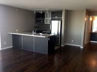 modern kitchen and living area featuring dark wood flooring, sleek black cabinetry, stainless steel appliances, and a spacious island with built-in sink, illuminated by track lighting and natural light from adjacent rooms, perfect for contemporary urban living.