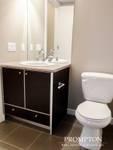 modern bathroom featuring a sleek dark wood vanity with a beige countertop, a clean white sink faucet, and a white toilet, all set against neutral beige walls and large floor tiles, creating a minimalist and tidy space with ample lighting.