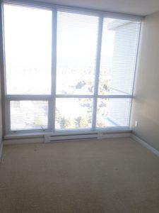 bright and spacious empty room featuring large floor-to-ceiling windows with horizontal blinds, beige carpet flooring, and neutral wall colors, offering abundant natural light and a clean, modern living space with a city view outside.