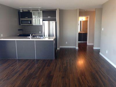 modern open-concept kitchen and living area featuring dark wood flooring, sleek black cabinetry, stainless steel appliances, and neutral gray walls, creating a clean and contemporary living space with natural light enhancing the warm ambiance.