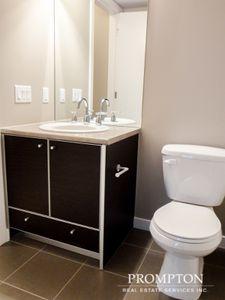 modern bathroom featuring a sleek dark wood vanity with a beige countertop, a clean white sink faucet, and a white toilet, all set against neutral beige walls and large floor tiles, creating a minimalist and tidy space with ample lighting.