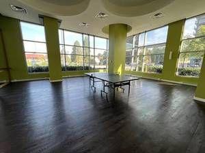 bright and spacious room with large windows offering abundant natural light, featuring dark wood flooring and minimalist decor with a ping pong table as the central focus, perfect for recreational or communal use in a modern building.
