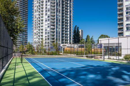outdoor tennis court with vibrant blue and green surface surrounded by tall modern residential buildings under a clear blue sky, offering excellent recreational amenities in an urban setting
