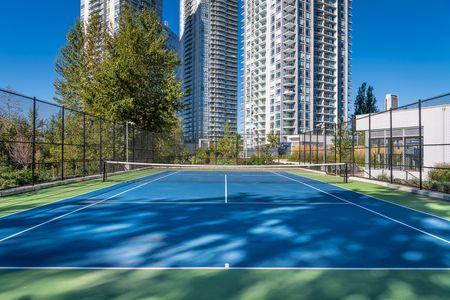 outdoor tennis court with blue and green surface surrounded by tall residential buildings and lush greenery under a clear blue sky, offering a premium urban recreational amenity in a modern high-rise community