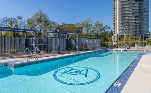 outdoor residential swimming pool with clear blue water and modern metal pergolas, surrounded by a secure fence and urban high-rise buildings under a clear blue sky, perfect for relaxation and recreation in a city setting